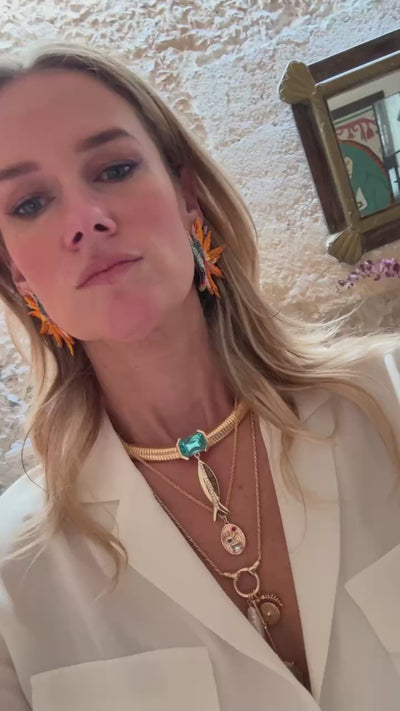 Model wearing orange beaded and embroidered earrings with a thick gold collar chain with bleu stone and fish pendant layered with gold necklaces