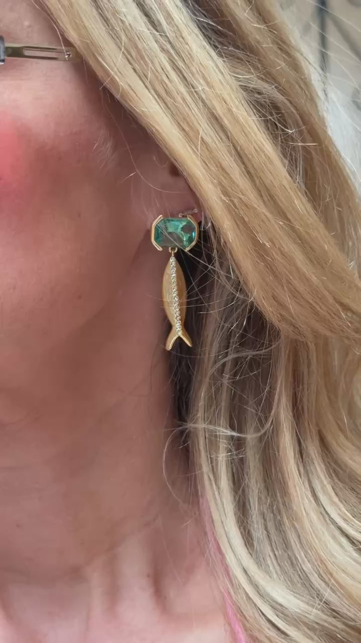 Model wearing blue glass stone earring with fish shaped gold and crystal drop on ear