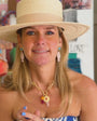 Model wearing a straw hat and blue dress while explaining the design begin the Liliana Charm earrings, pink fish shaped earrings with a blue stone topper