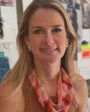 Model wearing gold, pink and orange gemstone stud earrings with a beaded scarf necklace around her neck while wearing a brown shirt and pink pants