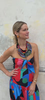 Model wearing sun shaped embroidered earrings with a beaded scarf necklace and colorful dress against stone background