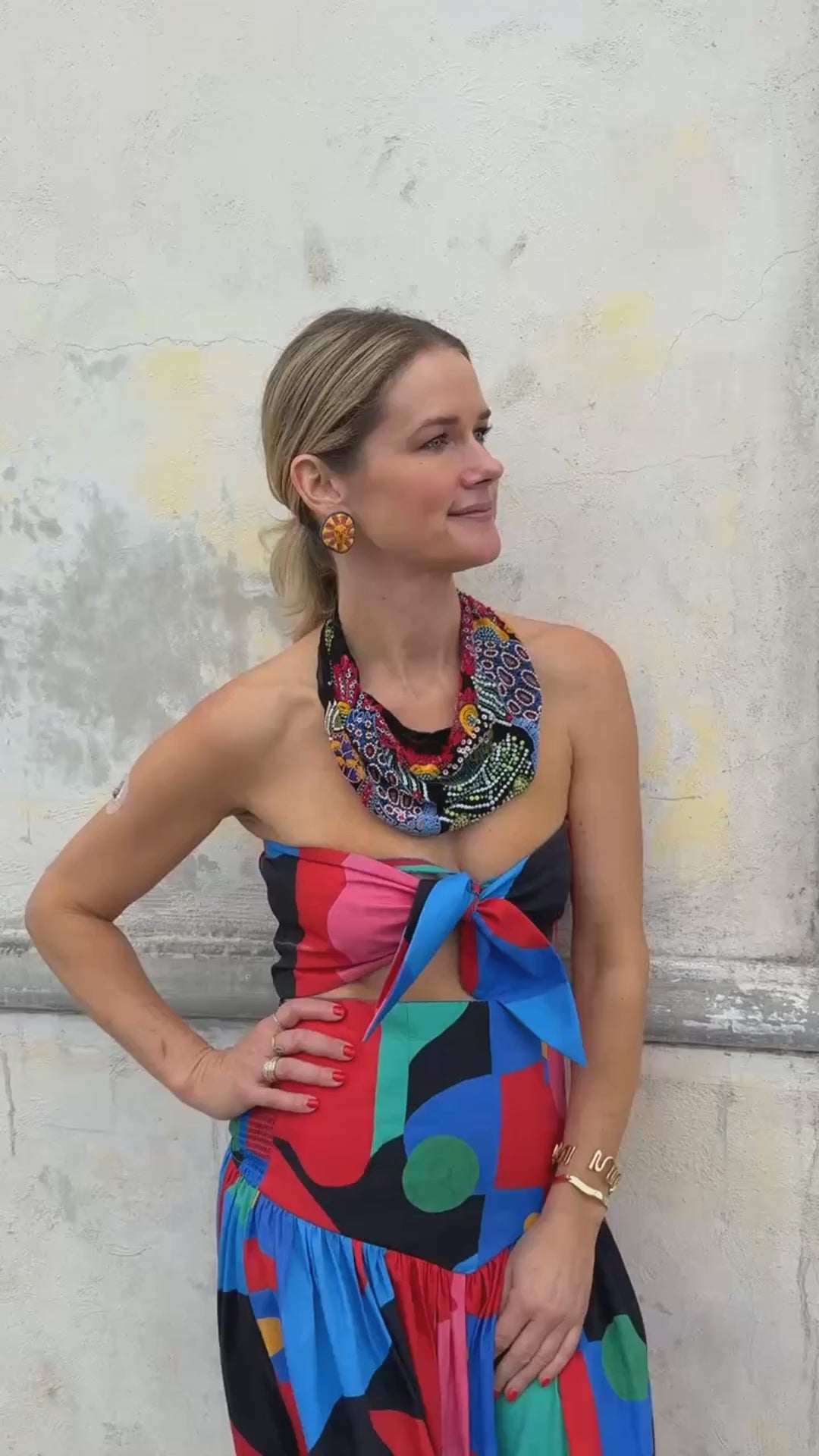 Model wearing sun shaped embroidered earrings with a beaded scarf necklace and colorful dress against stone background