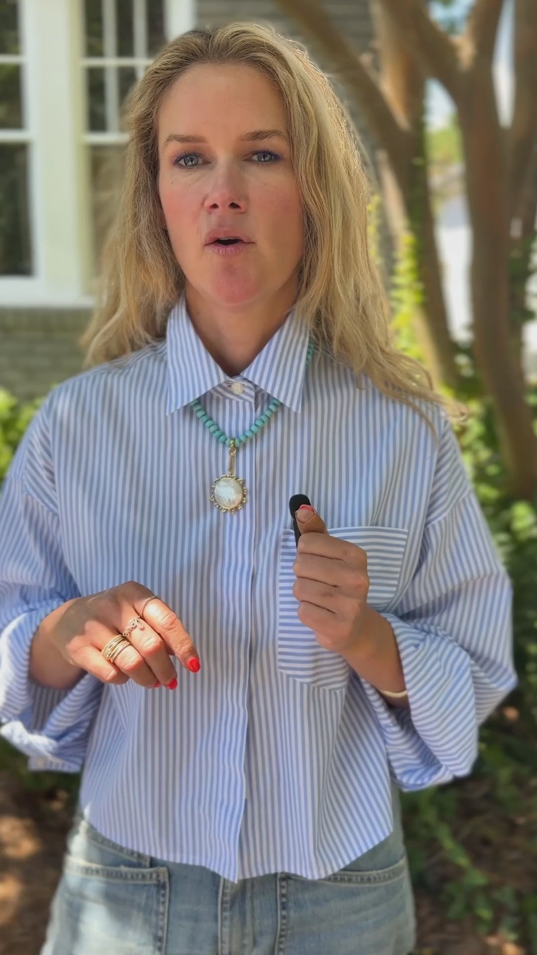 Model talking about a blue beaded necklace with a mother of pearl charm and highlighting the extender to show different neck lengths