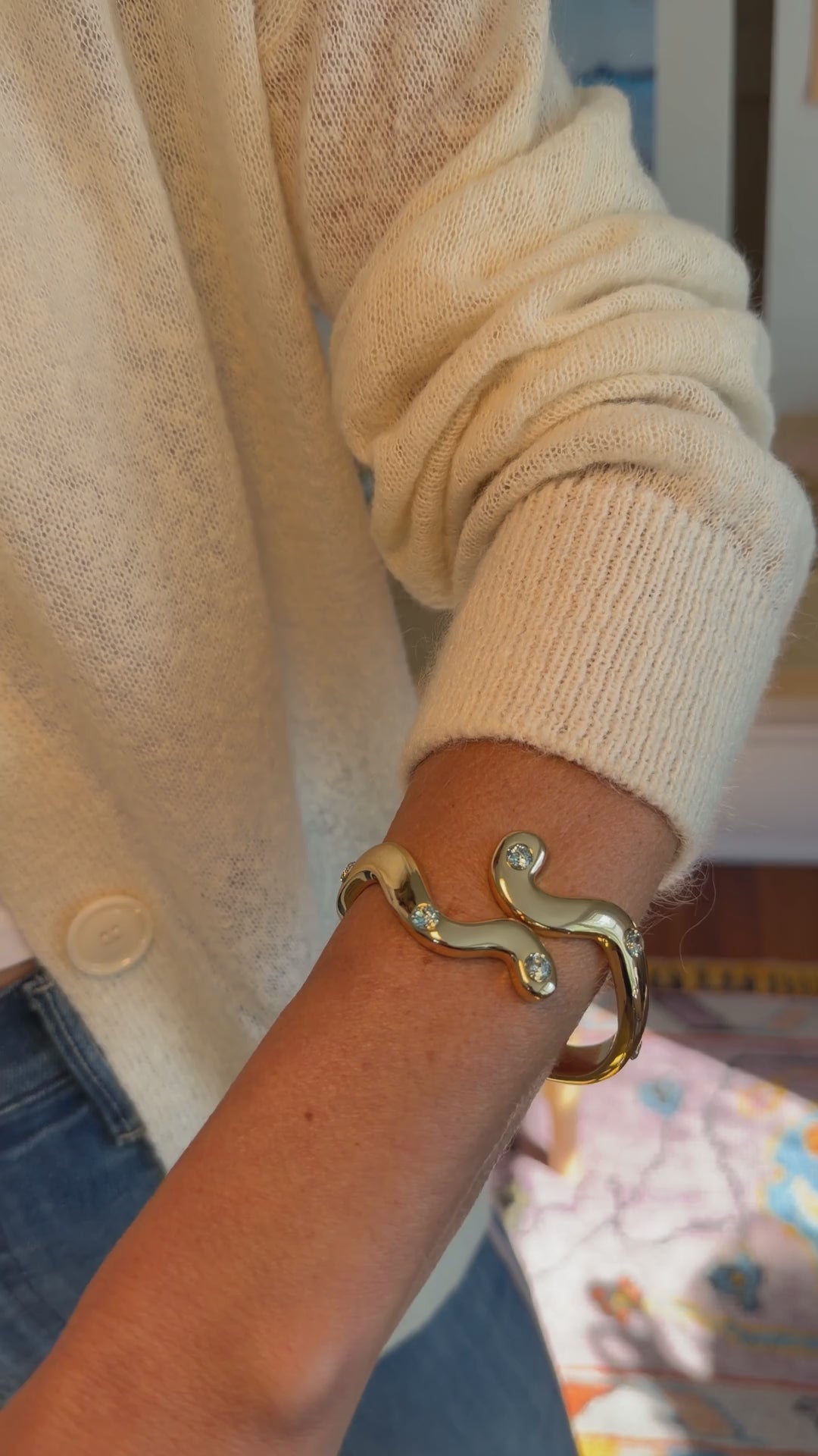 Model explaining a gold hinge cuff with blue stones around her write while wearing sweater and jeans