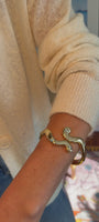 Model explaining a gold hinge cuff with blue stones around her write while wearing sweater and jeans