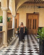 Woman walking down a hallway wearing a black dress with long chain gold necklace with a shell pendant
