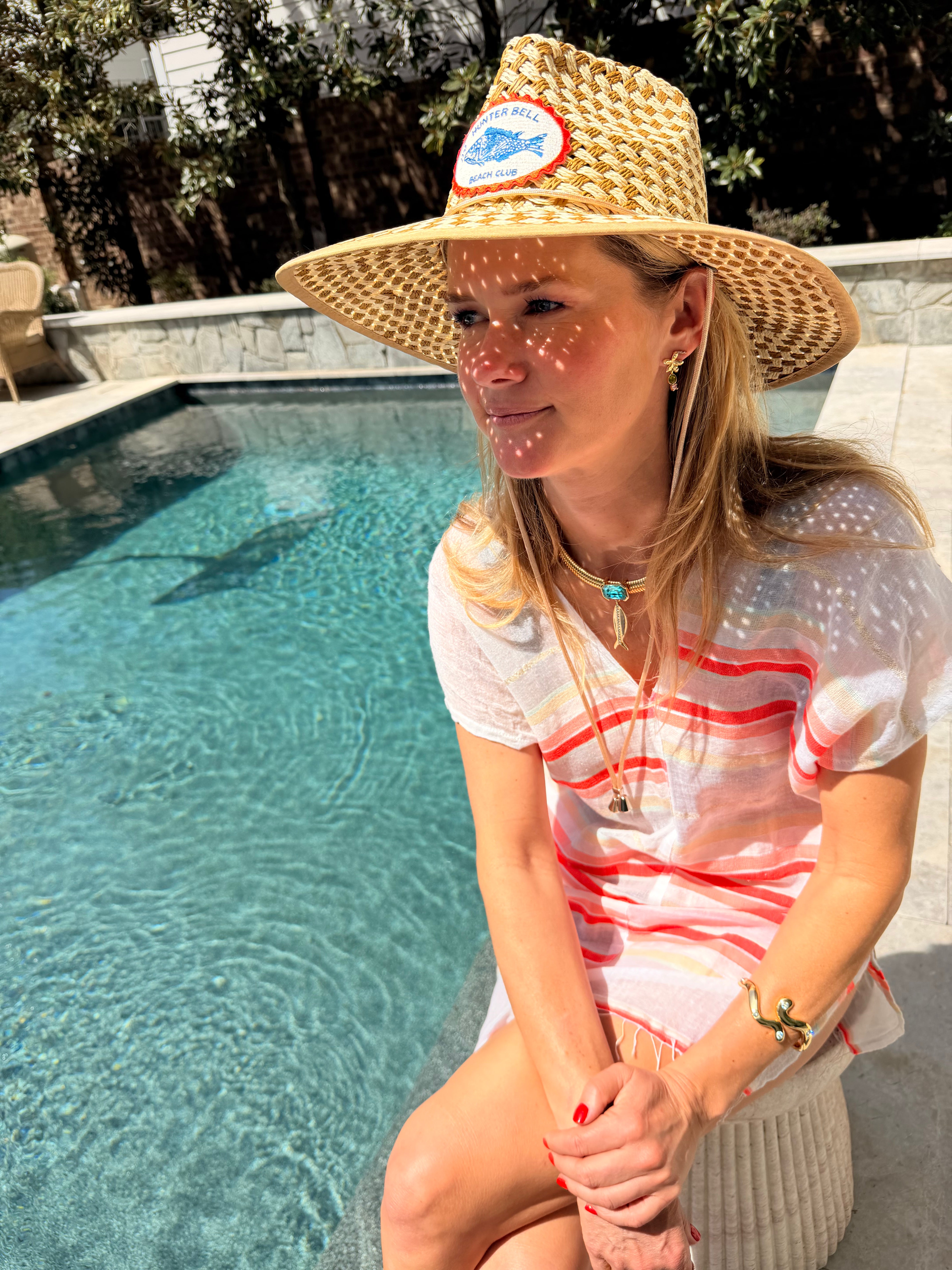 Model wearing staw hat and white and pink striped shirt near a pool showing off a palm tree shaped stud earrings