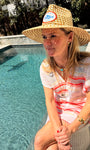 Model wearing staw hat and white and pink striped shirt near a pool showing off a palm tree shaped stud earrings