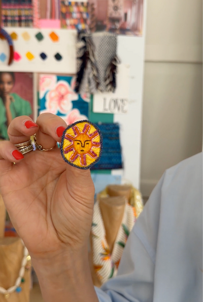 Video of model hold embroidered earring stud with a sun face on the against a mood board background