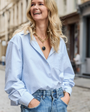 Model wearing blue dress button down shirt highlighting gold and black necklace in city streets