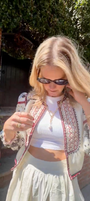 Model wearing bolero with white skirt explaining gold chain necklace with pearl drop charm outside
