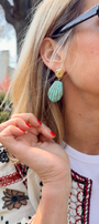Model outside explaining turquoise colored shell shaped drop earring 