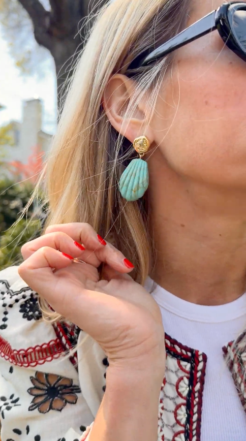 Model outside explaining turquoise colored shell shaped drop earring 