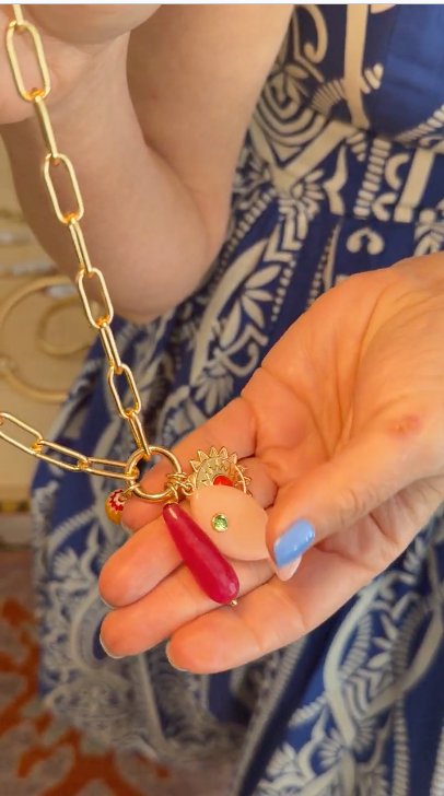 gold chain necklace with pink and orange fish charms while wearing a straw hat, blue dress and pink fish shaped drop earrings