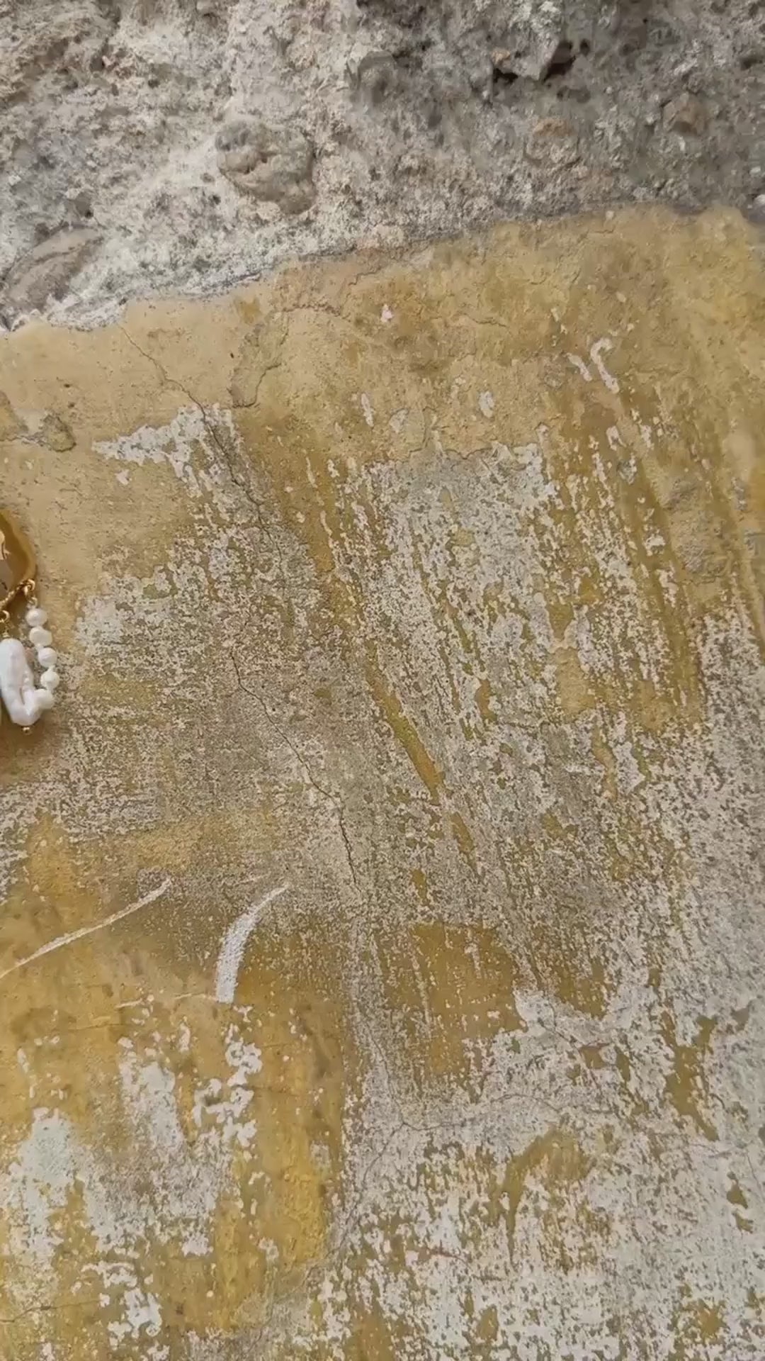 Video of a pair of gold and pearl drop earrings laying against a stone background