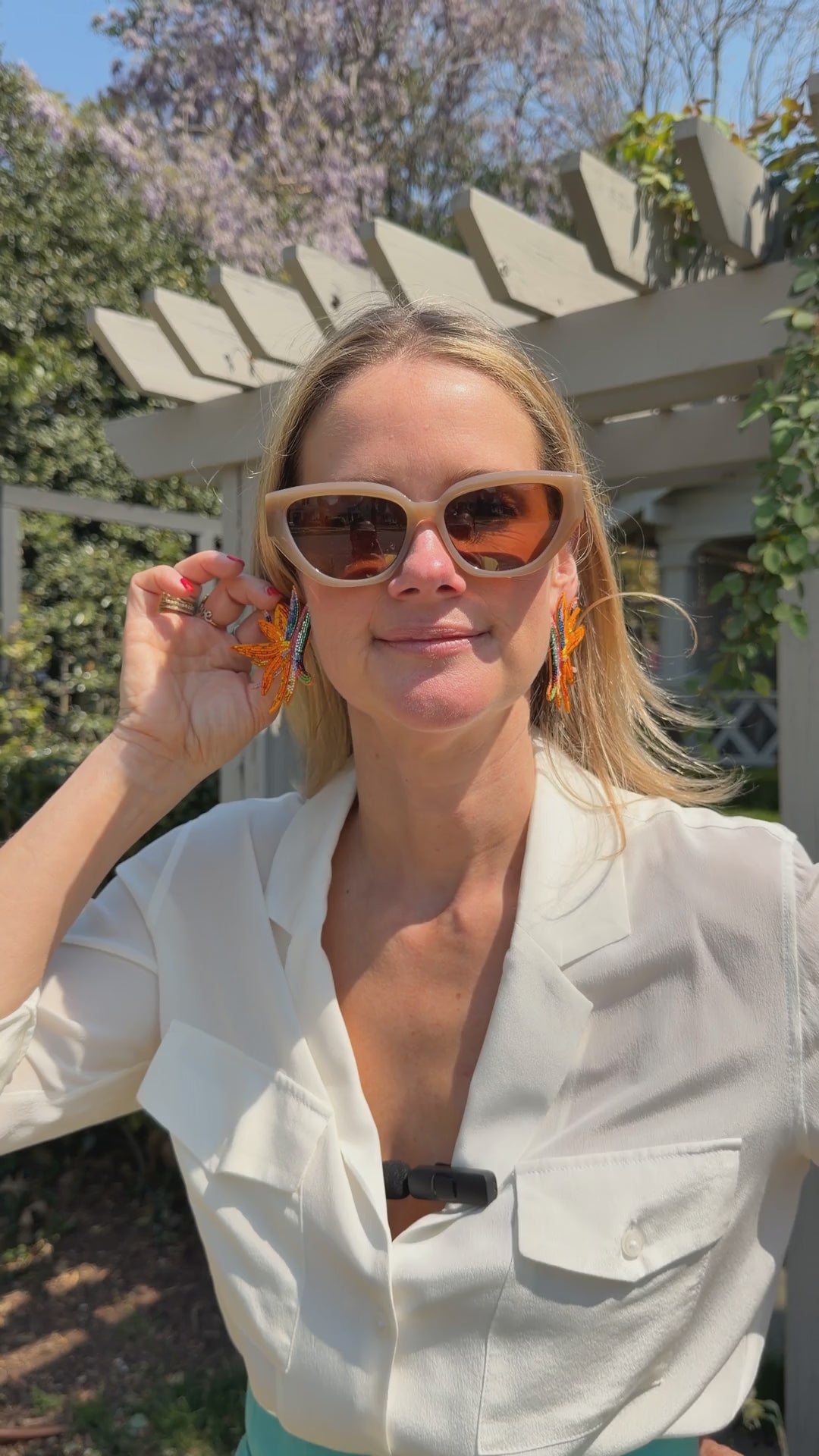 Model holding up bright orange embroidered bird earrings with white shirt on outside