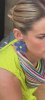 Model wearing blue floral shaped earring made with beads and threads while wearing a yellow dress and colorful scarf necklace