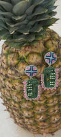 Alligator shaped earrings with green blue and pink accents resting on a pineapple against a white background