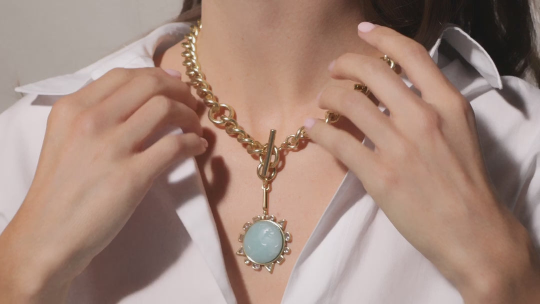 Load video: Person wearing a gold necklace with a blue pendant