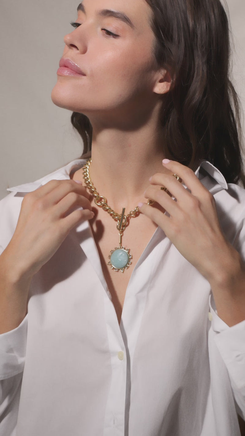 Person wearing a gold necklace with a blue pendant