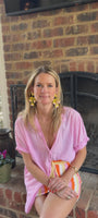 Model wearing yellow tulip shaped earrings in pink blouse and knit skirt against a fireplace