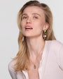 Blonde model wearing gold structured earrings and gold necklace on white background.