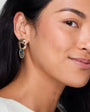 Close-up of a woman wearing a gold earring with a blue gemstone.