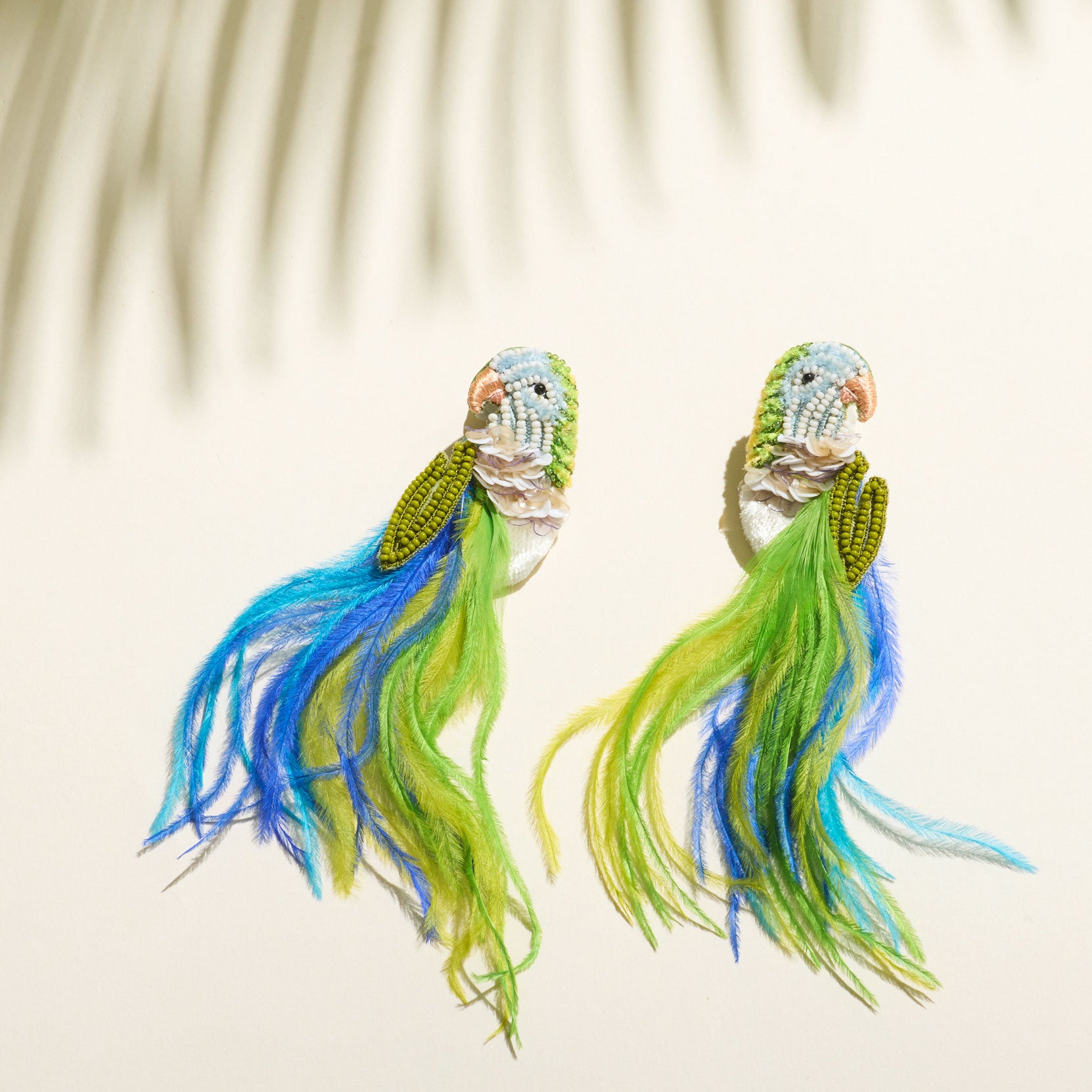 Blue, Green, and White Beaded and Feather Embroidered Bird Stud Earrings on Tan Background