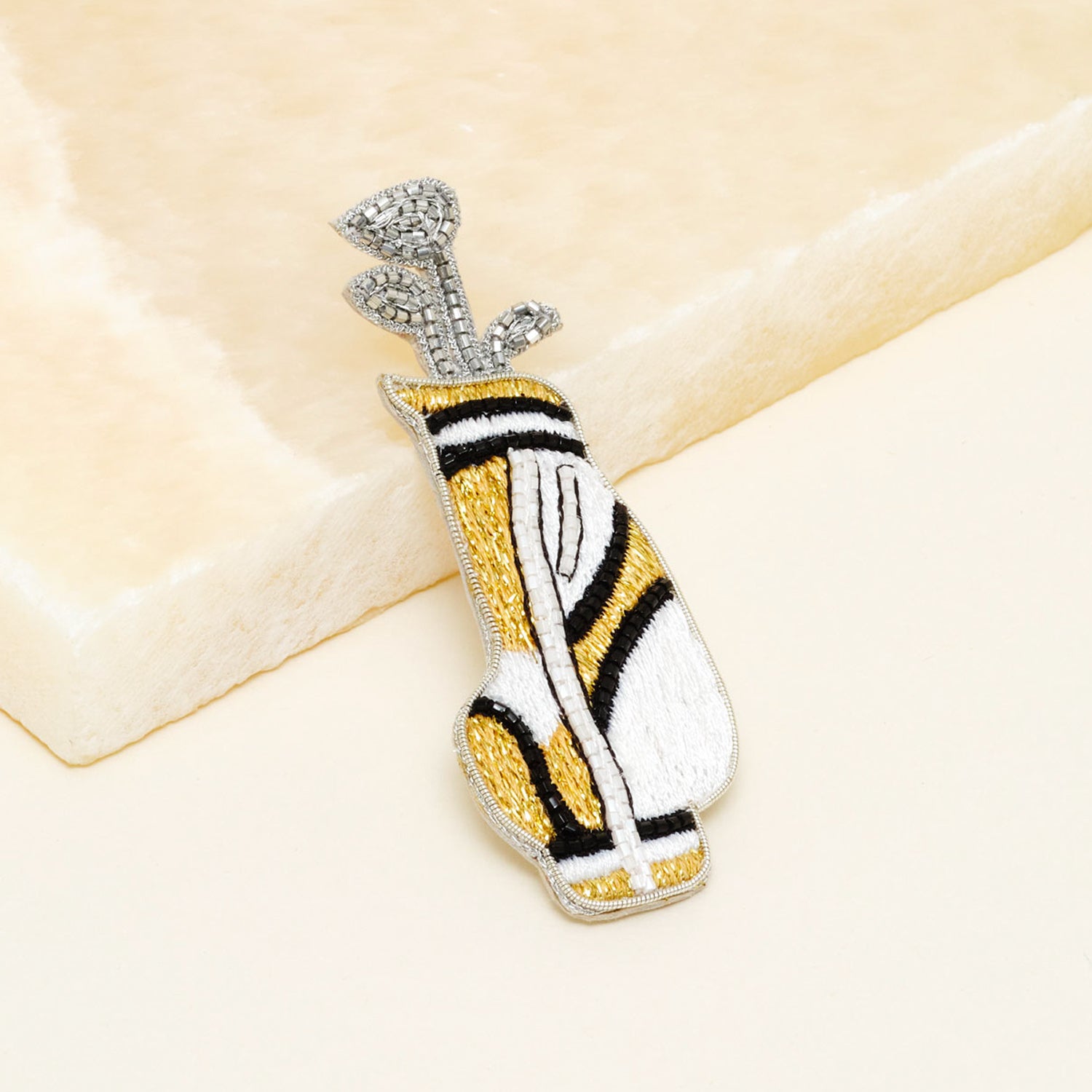 Gold, White, Black, and Silver Beaded Golf Bag Brooch on Tan Background